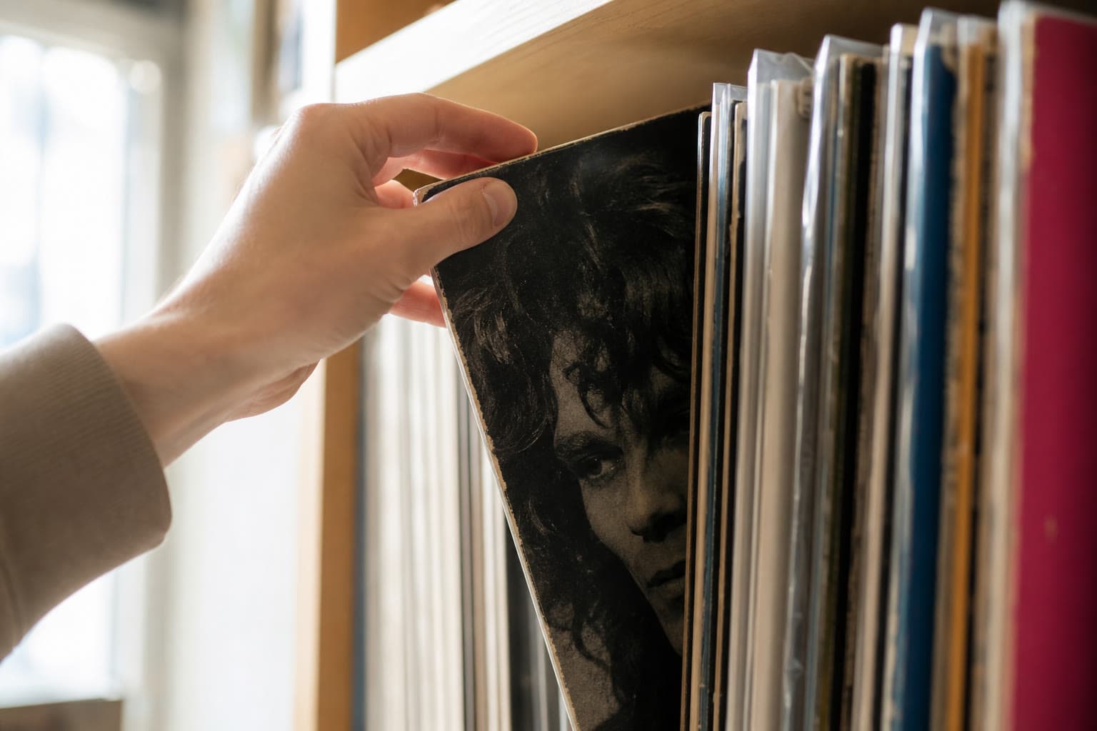 A hand drawing a vinyl record sleeve out of a tightly packed wooden shelf.