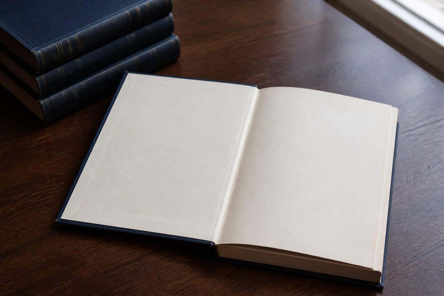 An open hardcover book on a wooden table with a stack of matching volumes beside it.